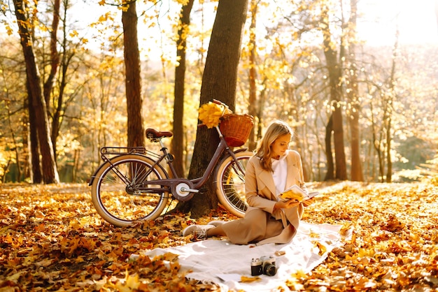 Bella joven sentada en unas hojas de otoño caídas en un parque leyendo un libro Relajación