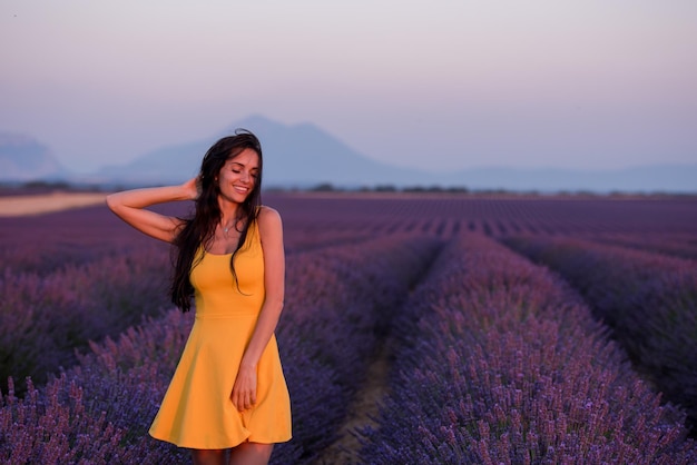 bella joven vestida de amarillo relajándose y divirtiéndose en el campo de lavanda de flores moradas