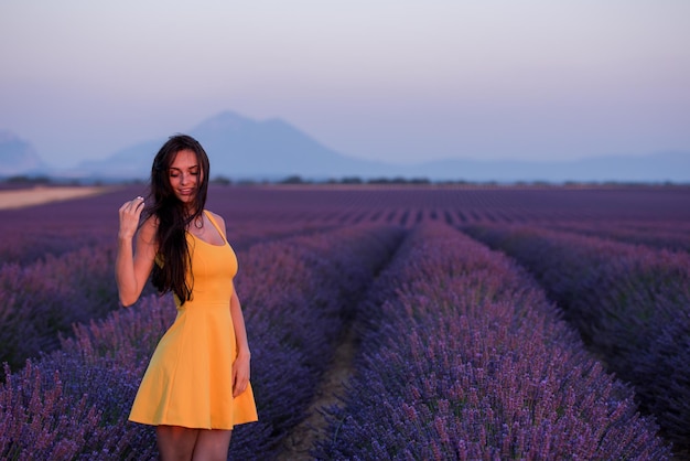 bella joven vestida de amarillo relajándose y divirtiéndose en el campo de lavanda de flores moradas