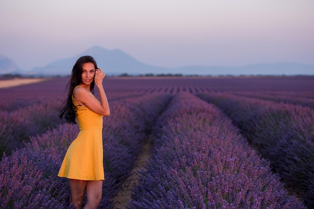 bella joven vestida de amarillo relajándose y divirtiéndose en el campo de lavanda de flores moradas