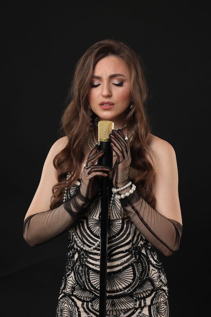 Bella joven con un vestido elegante con micrófono cantando sobre un fondo negro
