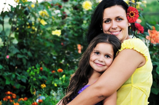 bella madre e hija al aire libre en el jardín junto con flores se divierten y se abrazan