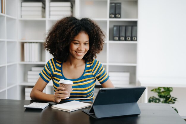 Bella mujer africana usando portátil y tableta mientras está sentada en su lugar de trabajo concentrada en la oficina de casa