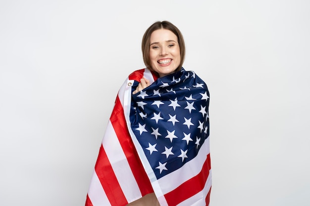 Bella mujer afroamericana sonriente cubierta con bandera estadounidense aislada sobre un fondo blanco