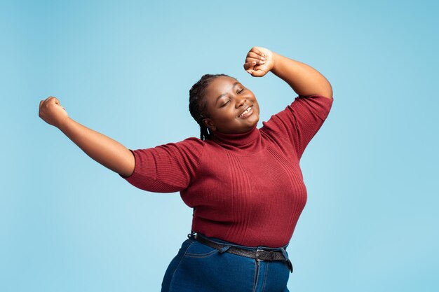 Bella mujer afroamericana sonriente de tamaño grande con ropa casual con los ojos cerrados bailando