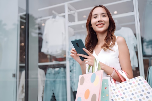 Bella mujer asiática con bolsas de compras Caminar disfrutando de sonreír mientras hace compras fuera de los centros comerciales ventana al aire libre estilo de vida de moda