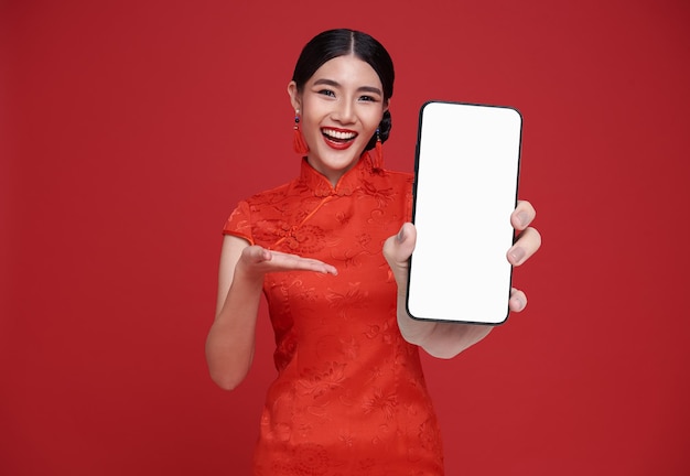 Bella mujer asiática china feliz sosteniendo una maqueta de teléfono inteligente y señalando con el dedo la pantalla en blanco