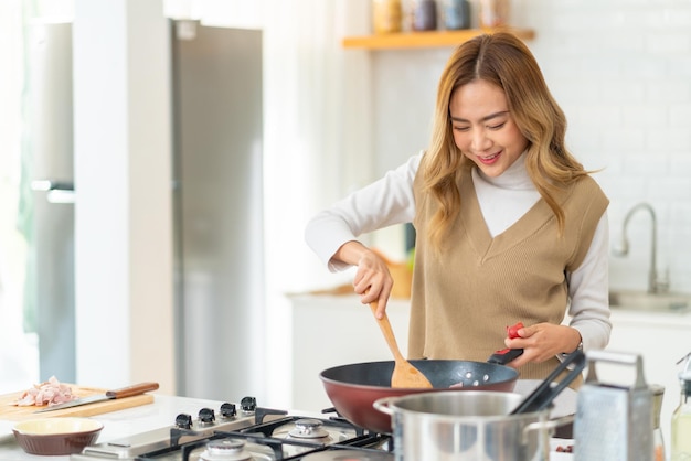 Bella mujer asiática disfruta cocinando comida saludable pasta y filete de salmón en la sartén de cocción en la cocina en casa feliz mujer teniendo cena fiesta reunión celebración con amigos en vacaciones vacaciones