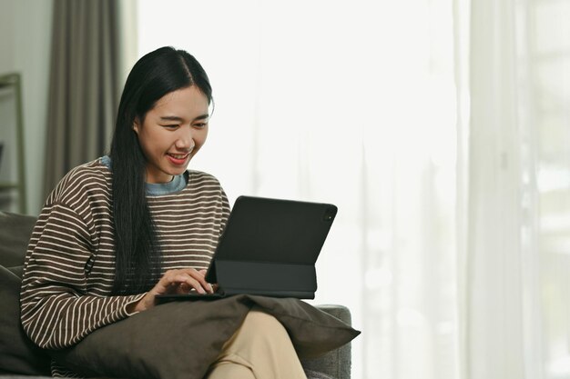 Bella mujer asiática hablando en una tableta digital navegando por Internet o trabajando en línea en casa