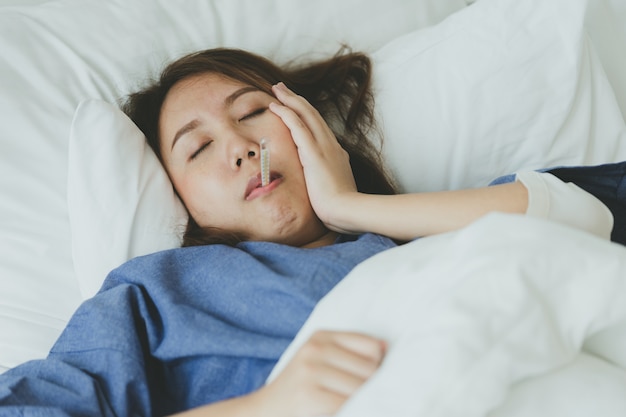 La bella mujer asiática Hipotermia ha sido medida por la fiebre. Acostado en la cama