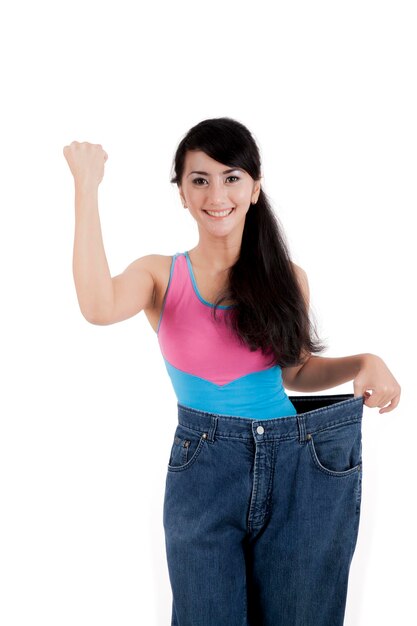 Foto bella mujer asiática mostrando su pérdida de peso con pantalones vaqueros viejos aislados sobre blanco