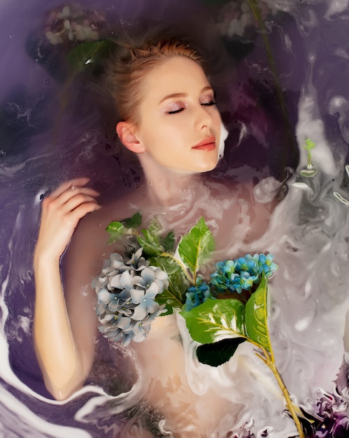 Bella mujer en bañera con flores y agua púrpura