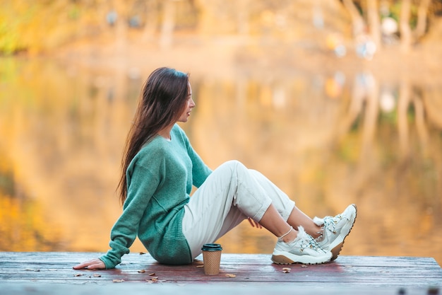 Bella mujer bebiendo café en el parque de otoño bajo el follaje de otoño