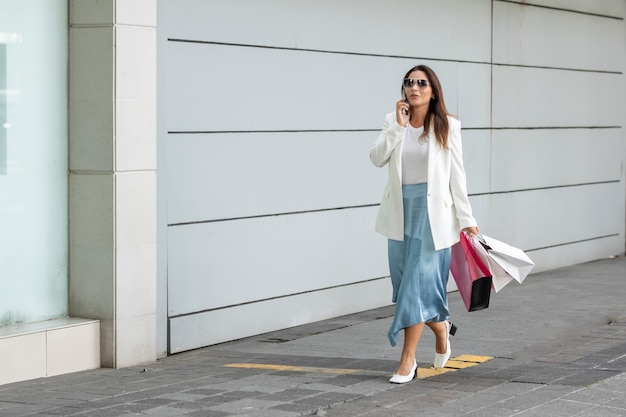 Bella mujer con bolsas de la compra caminando por la calle mientras habla por teléfono