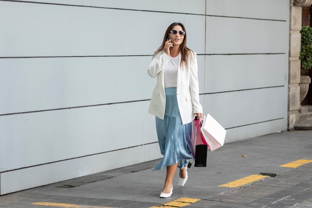 Bella mujer con bolsas de la compra caminando por la calle mientras habla por teléfono