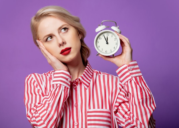 Bella mujer en camisa de rayas rojas con reloj despertador