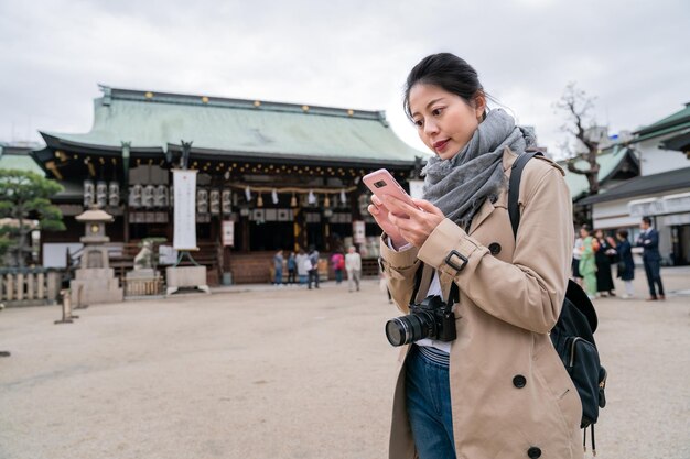 bella mujer cargando su cámara, parada frente al templo y charlando con su amiga por celular