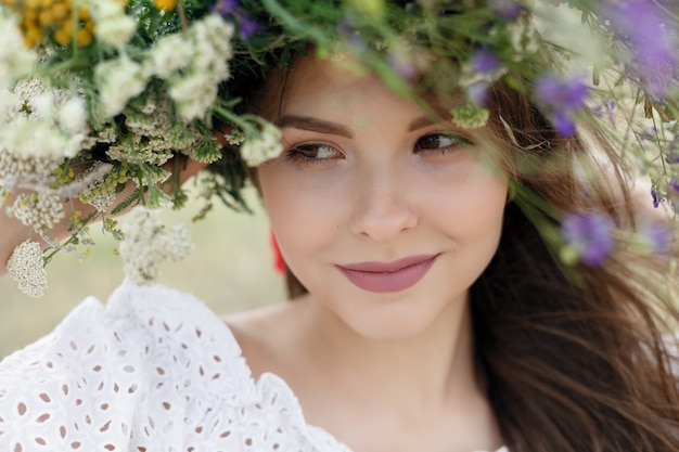 Bella mujer con corona de flores en la cabeza. Chica de belleza con peinado de flores. Chica en un bosque de verano. Foto de moda