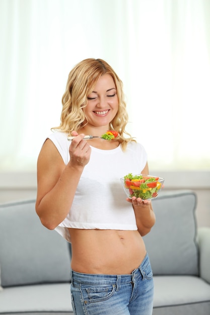 Bella mujer con ensalada en el interior de una casa