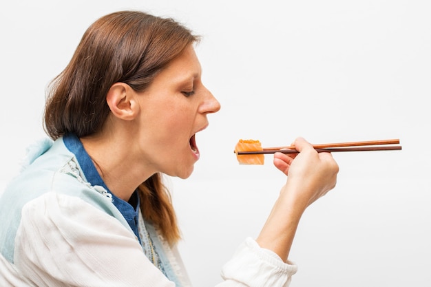 Bella mujer está comiendo sushi con palillos de madera