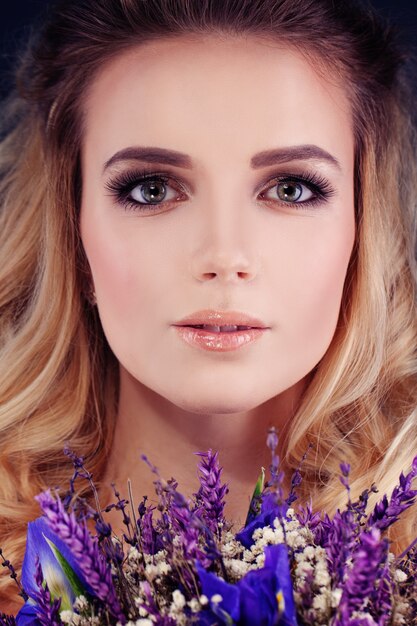 Bella mujer con flores. Primer lindo de la cara. Maquillaje y peinado rubio