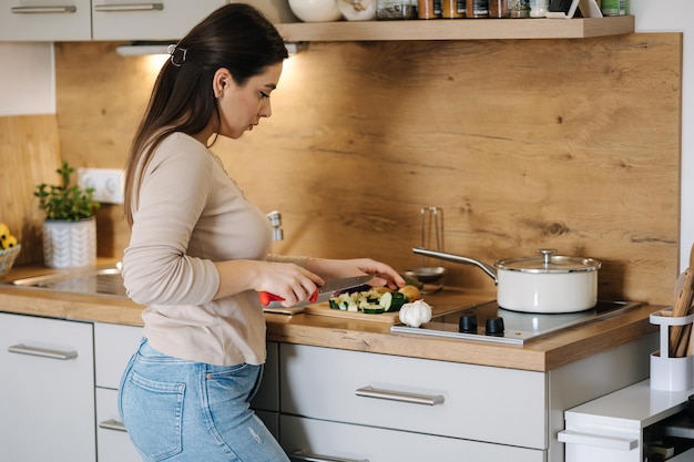 Bella mujer joven cortando verduras en la cocina en el concepto de comida en el hogar