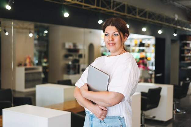 Foto bella mujer joven elegante más tamaño cuerpo positivo con computadora portátil en la oficina del salón de belleza