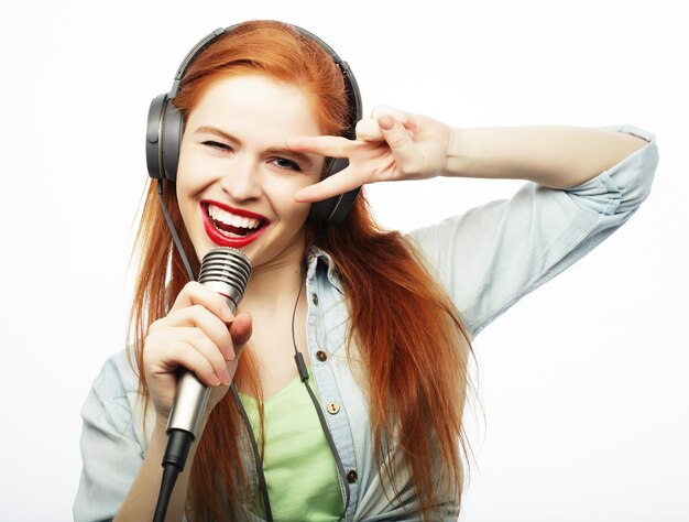 Bella mujer joven con micrófono y auriculares en fondo gris