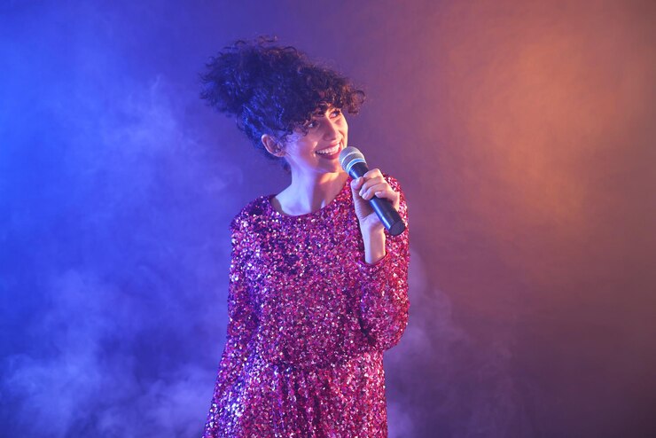 Foto bella mujer joven con micrófono cantando en fondo de color en luces de neón y humo