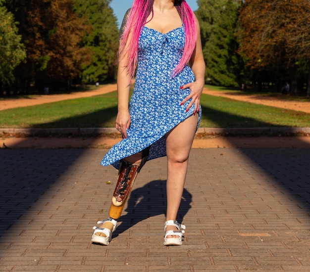 Bella mujer joven con la pierna amputada en un vestido caminando en el parque en un día soleado