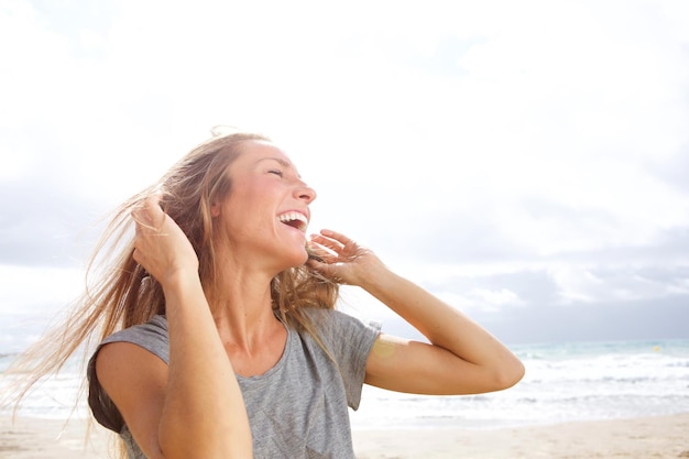 Bella mujer joven riendo en la playa con la mano en el cabello