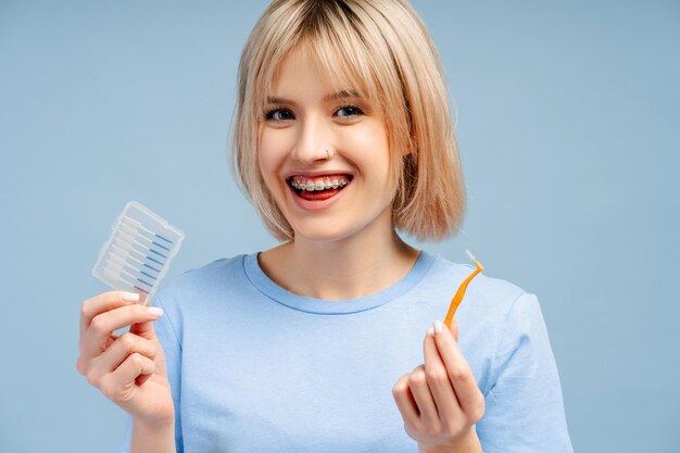 Foto bella mujer joven sonriente con aparatos ortopédicos usando un pincel interdental mirando a la cámara