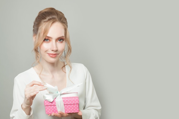 Bella mujer joven sosteniendo una caja de regalo rosa y sonriendo