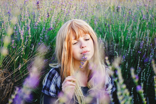Bella mujer joven sosteniendo flores de lavanda mientras está sentada en el campo de lavanda