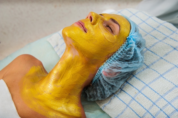 Bella mujer con máscara de oro facial en el salón de belleza