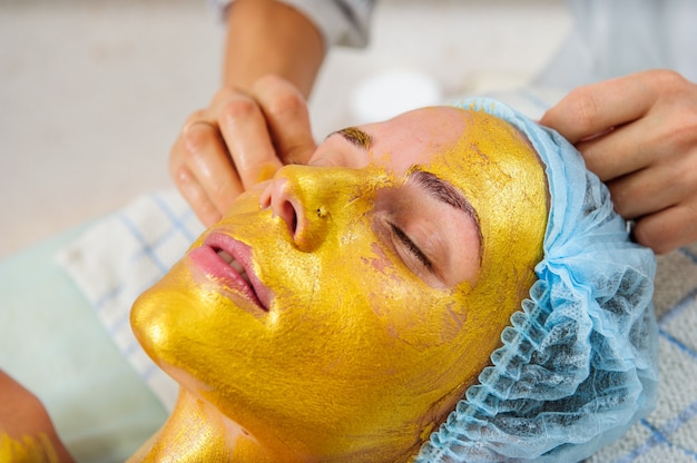 Bella mujer con máscara de oro facial en el salón de belleza