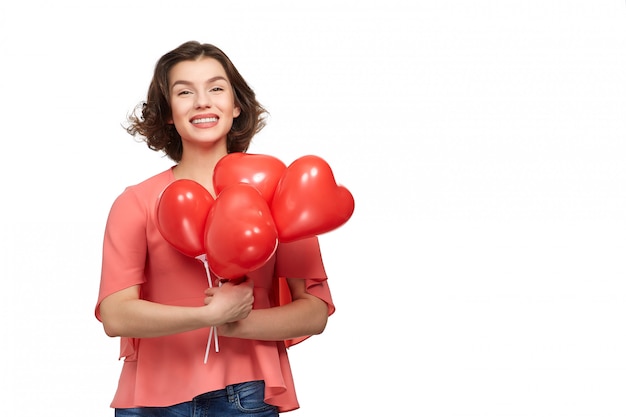 Una bella mujer morena con una amplia sonrisa en jeans y una chaqueta rosa con globos rojos en forma de corazón