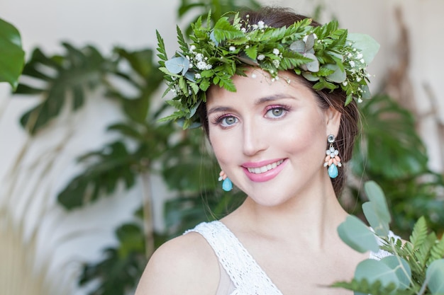 Bella mujer morena con flores y hojas verdes corona sonriendo en hojas verdes de fondo