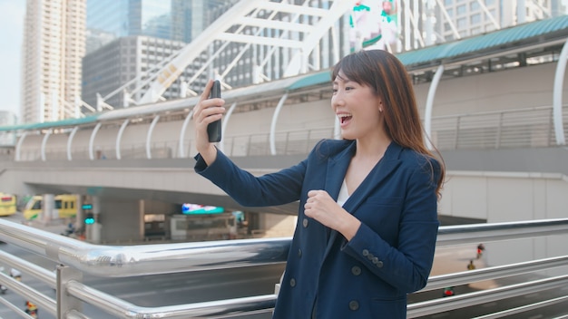 Una bella mujer de negocios asiática está haciendo videollamadas con colegas o familiares en la ciudad moderna, la cooperación empresarial y el concepto de tecnología empresarial.