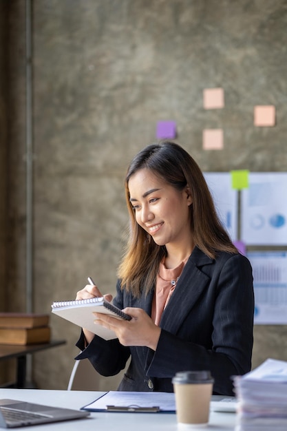 Una bella mujer de negocios asiática sentada en su oficina privada está revisando los documentos financieros de la empresa. Es una ejecutiva de una empresa nueva. Concepto de gestión financiera.