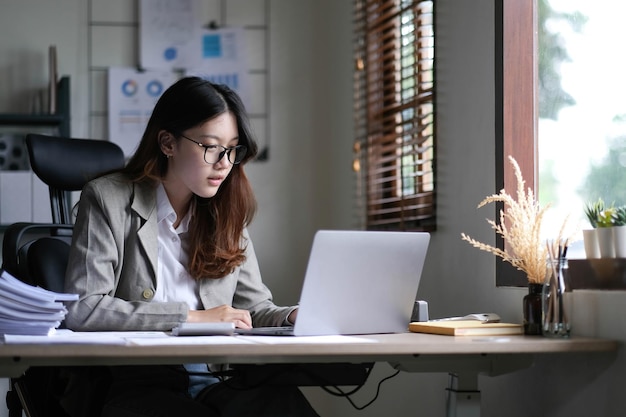 Bella mujer de negocios asiática sentada trabajando en una computadora portátil en la oficina