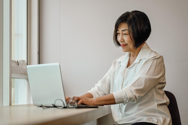 Bella mujer de negocios senior leyendo correo electrónico o buscando información en la computadora portátil en el escritorio