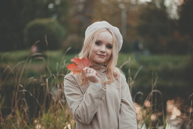 Bella mujer rubia con hojas de arce de otoño rojas en el fondo de otoño