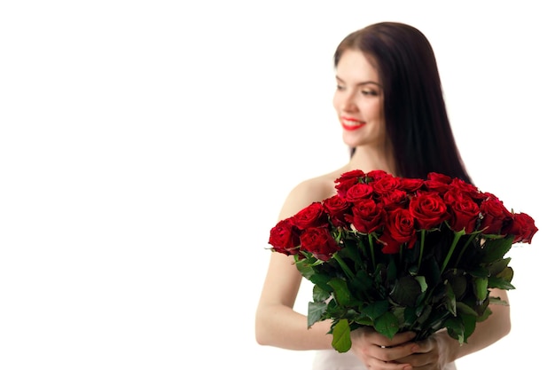 Bella mujer sonriente en vestido blanco con ramo de rosas rojas sobre fondo blanco. centrarse en las rosas. día de San Valentín