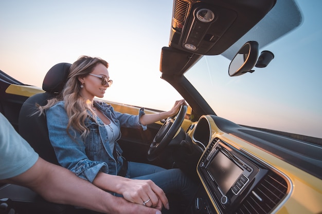 La bella mujer con su hombre viaja en un descapotable