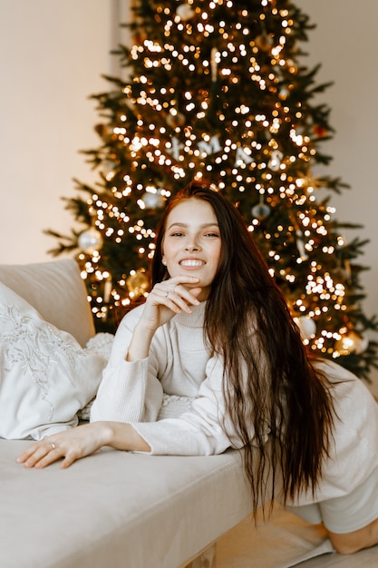 Bella mujer en un suéter de invierno blanco en el fondo de un árbol de Navidad