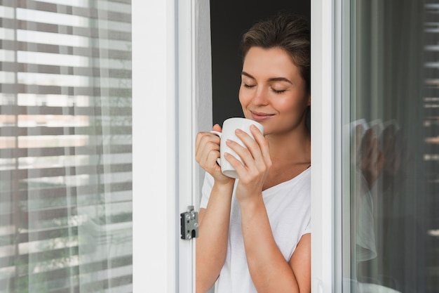 Bella mujer con una taza de café caliente mirando por la ventana