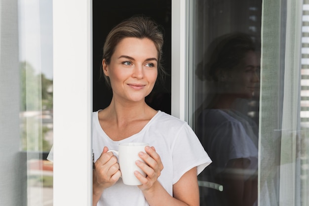 Bella mujer con una taza de café caliente mirando por la ventana