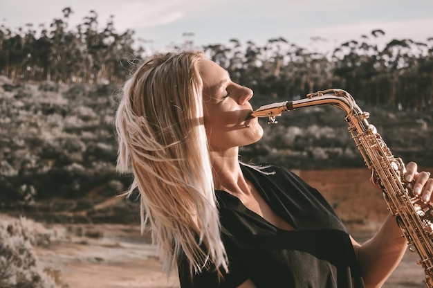 Bella mujer tocando el saxofón contra el árbol