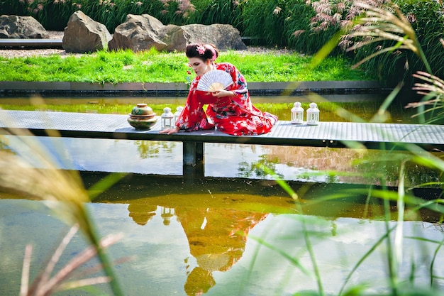 Bella mujer en traje de geisha en el jardín en el puente